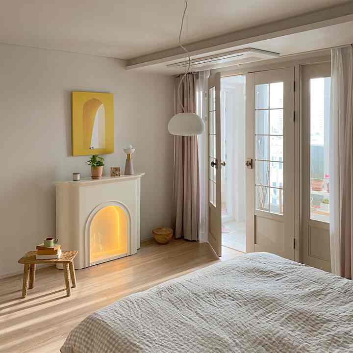 Cozy bedroom with soft beige and wood tones, featuring a fireplace console and pendant light in a natural modern interior