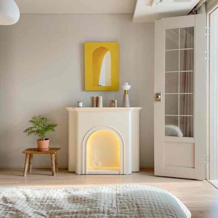 Natural modern bedroom with white and yellow accents, featuring a fireplace and plant creating a cozy atmosphere