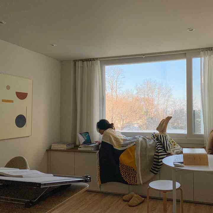 Cozy home office with white and wood tones featuring a window nook where a person works remotely on a laptop