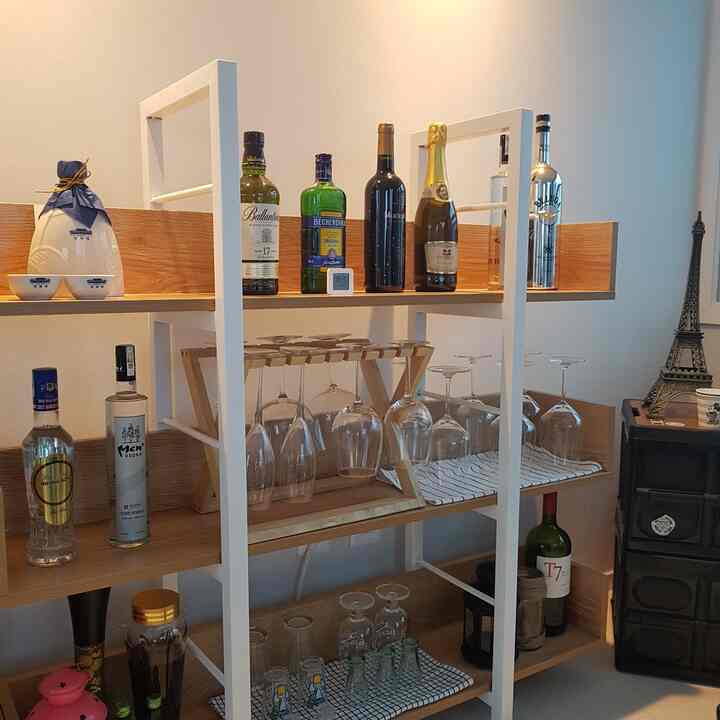 白いフレームと木目調の棚が特徴の小さなホームバー、様々な酒瓶とワイングラスが整然と置かれたインテリア