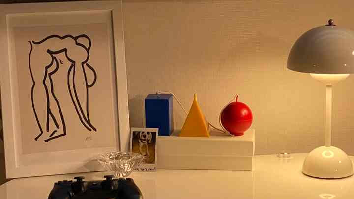 Cozy living room corner with white table featuring Henri Matisse poster, colorful candles, and table lamp under warm lighting