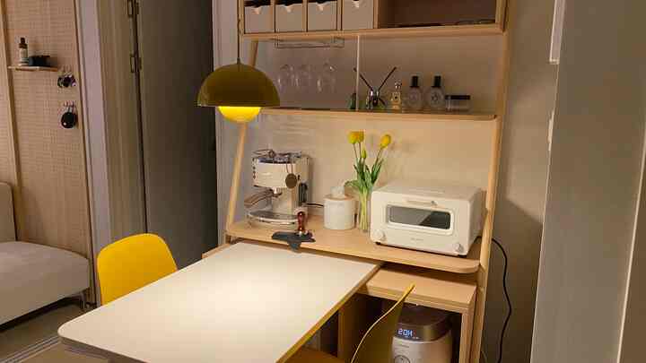 黄色の照明が印象的なコンパクトなキッチンダイニング、ミニマルでモダンな家具とホームカフェ機器が配置された空間