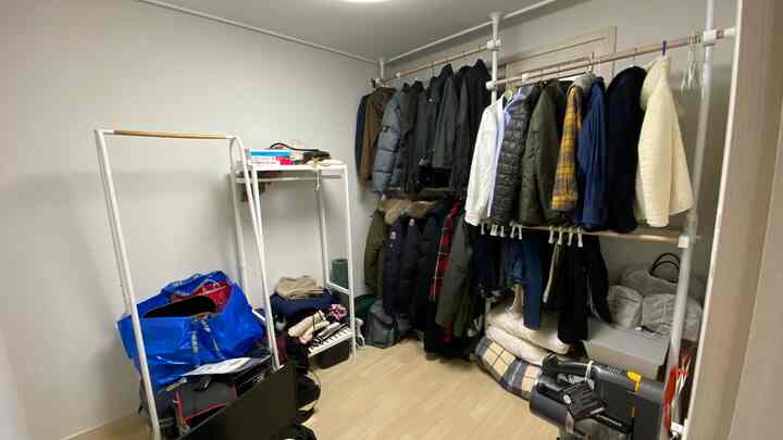 Small walk-in closet with white walls and wood-tone flooring, featuring two clothing racks densely filled with layered winter jackets