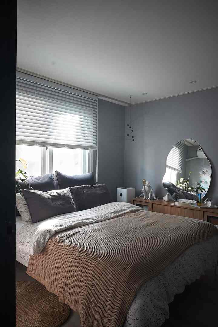 Gray-toned bedroom featuring a wood tone dresser and cozy bed with brown blanket and multiple pillows