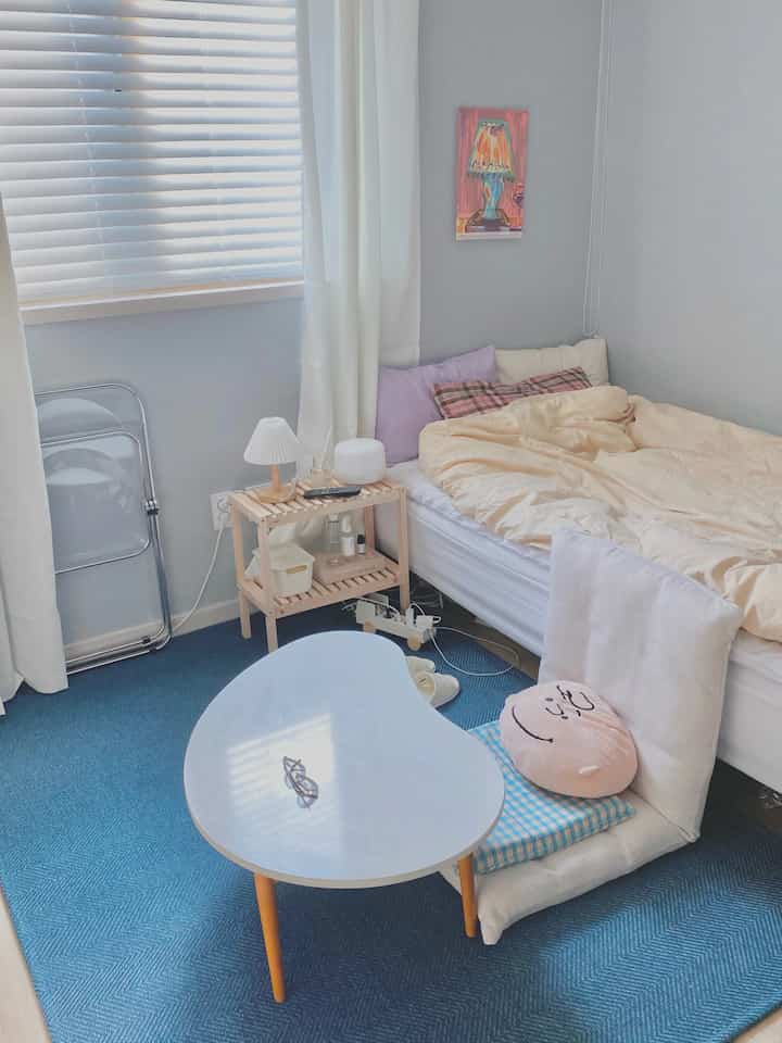 Pastel-toned bedroom with blue rug featuring a low table and floor chair, creating a cozy atmosphere