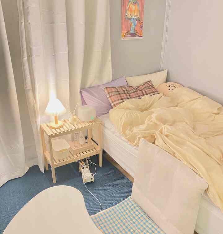 Ivory and beige toned bedroom featuring natural wood nightstand with mood light, navy rug, and floor chair creating cozy atmosphere