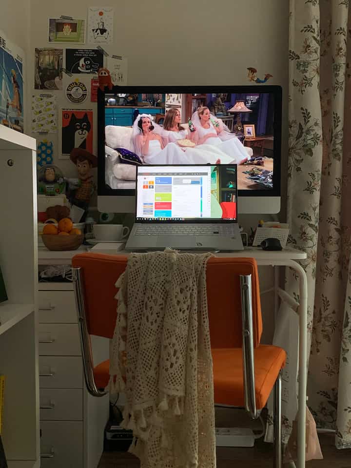 白とオレンジのトーンのホームオフィス、デスク上のノートパソコンとヴィンテージなファブリックが配置された雰囲気のある作業空間