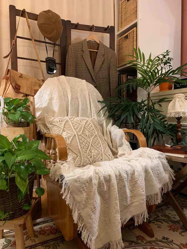 Cream and beige natural-toned bedroom featuring a wooden rocking stool with macramé cushion and various plants, creating a cozy atmosphere