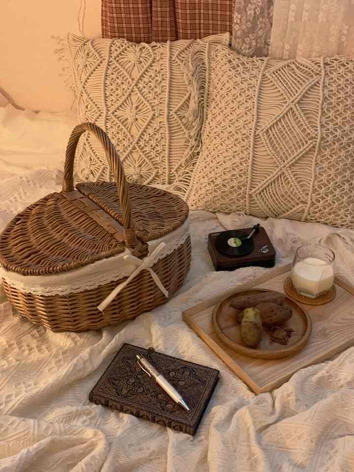 Natural tone bedroom featuring rattan basket, macrame cushions, blanket, wooden plate with warm sweet potatoes and milk in cozy setting