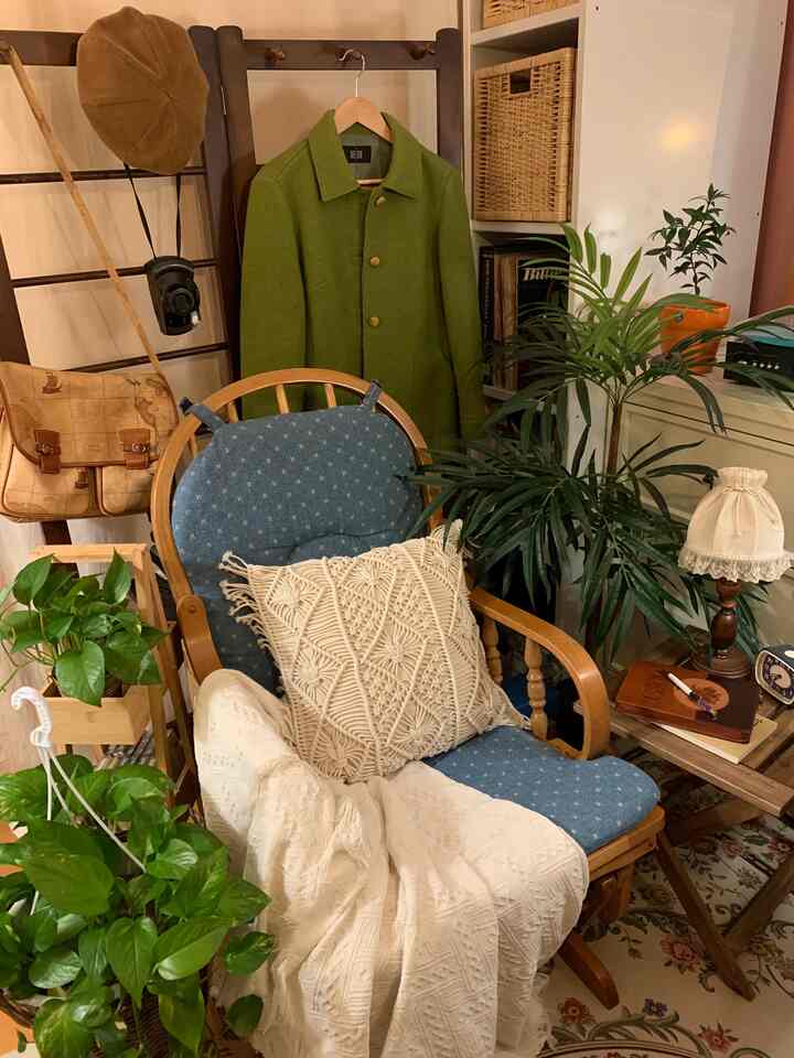 A bedroom featuring green and wood tones with a wooden rocking chair, macrame cushion, and various plants creating a natural vintage atmosphere