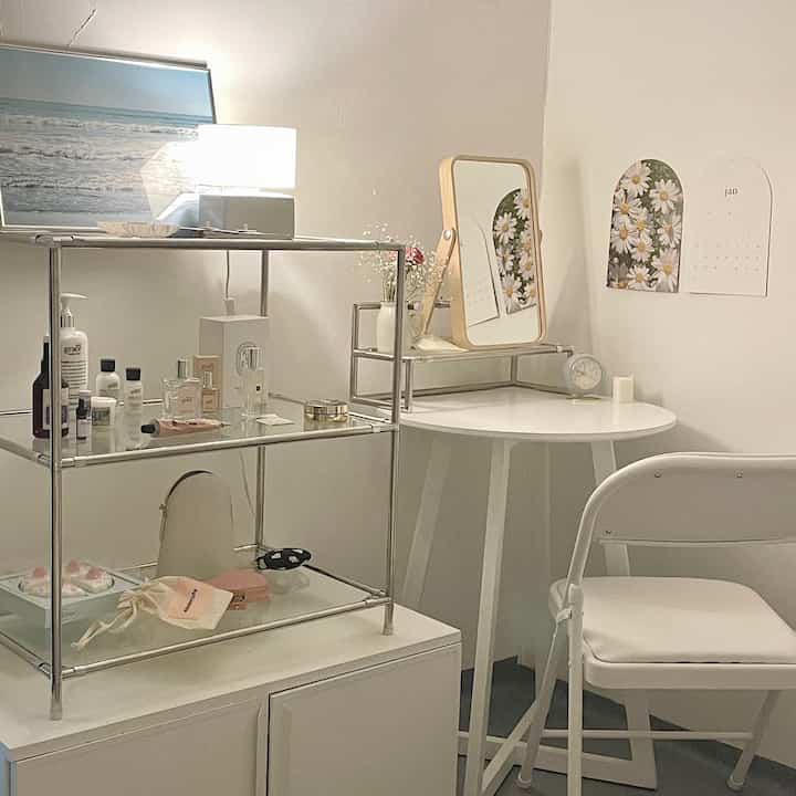White and silver toned small room featuring a vanity with mirror and shelving, arranged in a simple, clean interior