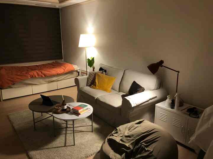 ベージュとオレンジの色調のワンルーム、ホワイトソファとシンプルな家具が配置された落ち着いたインテリア