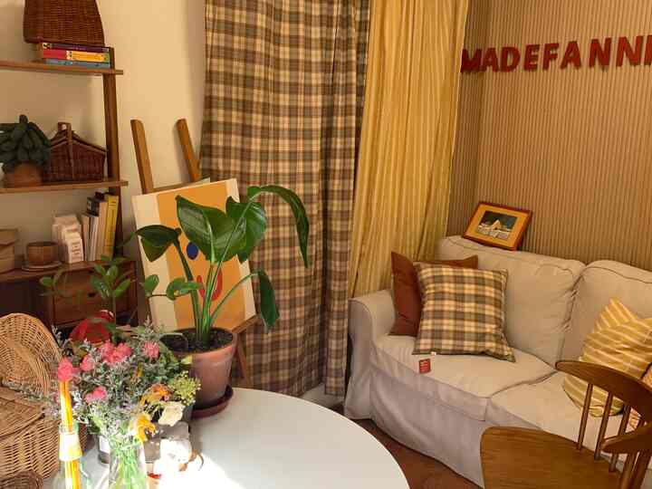 A warm living room with yellow and beige tones featuring a white sofa, round dining table, cushions, and plants in a cozy setting