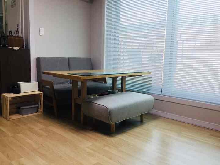 ナチュラルな色調のリビング、木製のダイニングテーブルとグレーのソファ、低いベンチが配された清潔感のある広々とした空間