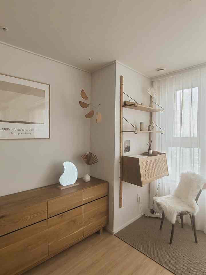 Natural tone small room featuring wood tone cabinet and shelves, white curtains and a fluffy chair with cozy atmosphere