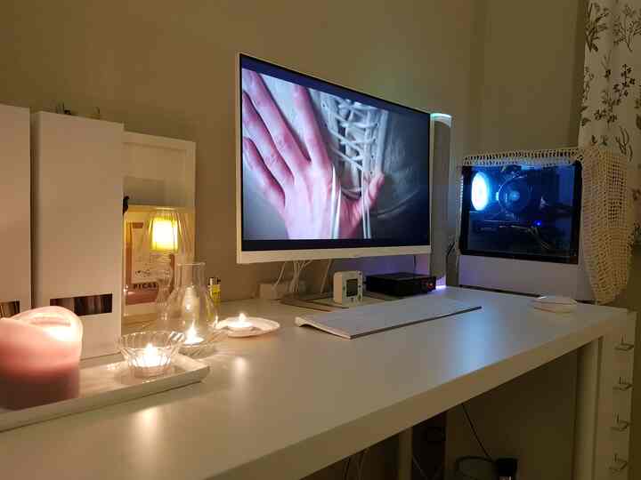 Cozy white-toned home office with warm lighting, features a white desk with a monitor and illuminated PC case