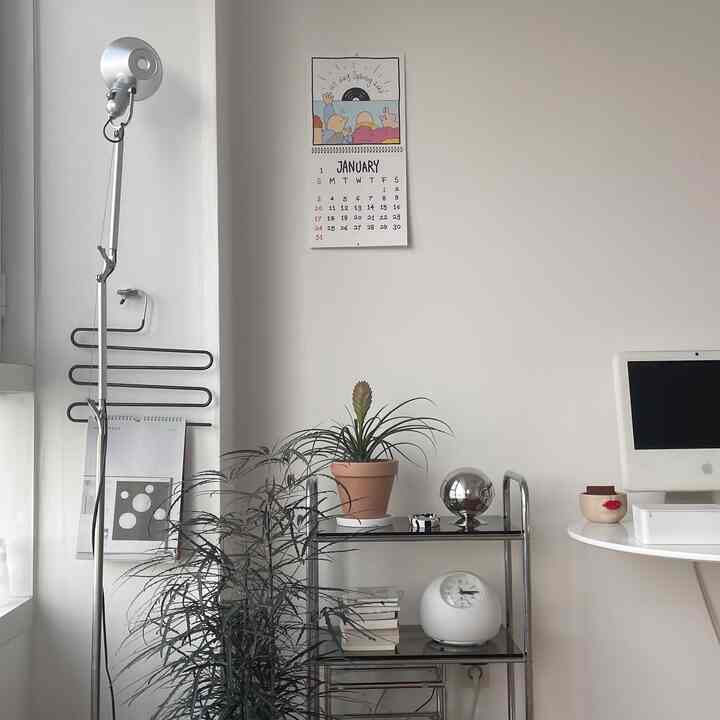 明るい白い壁とシルバーの棚があるワンルーム、植物とシンプルな丸型デスクが配されたミニマルな雰囲気のインテリア