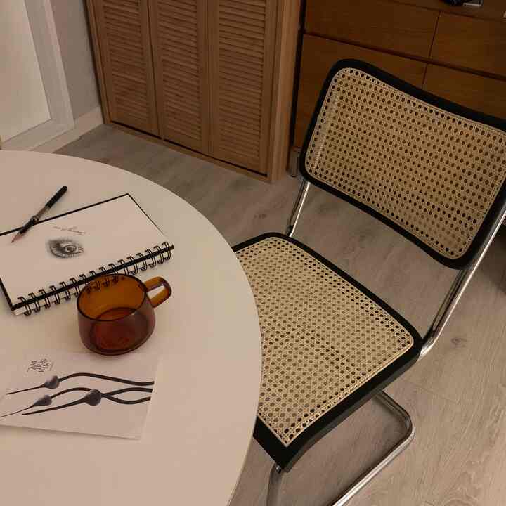 White-toned studio apartment dining area featuring rattan chair and wooden storage cabinet with cozy modern atmosphere