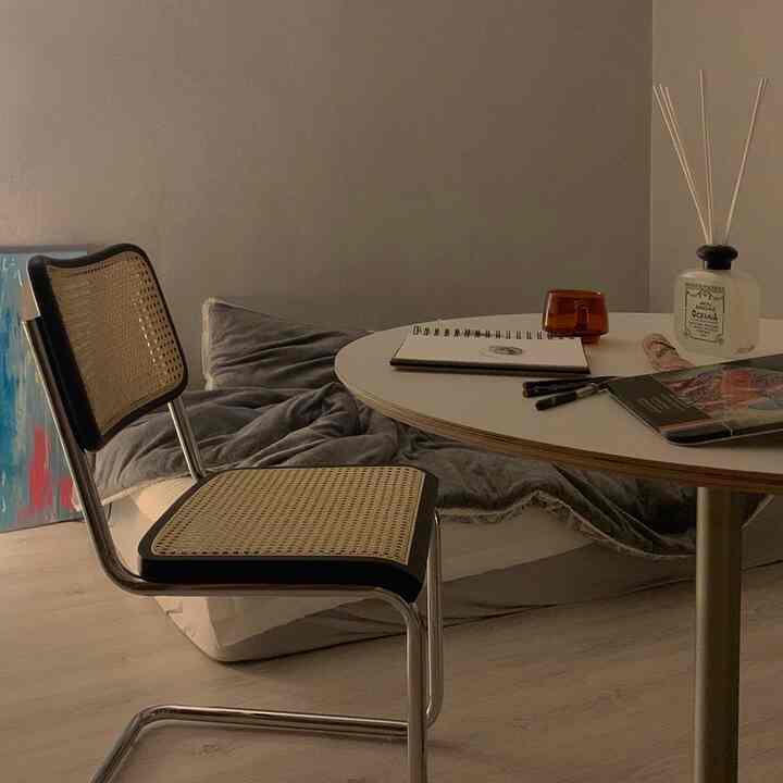 Natural-toned compact studio featuring a rattan chair, round table, and low mattress with a cozy home office vibe