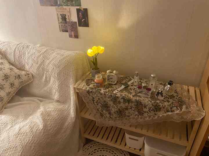 Beige-toned wall and natural wood shelf in a living room featuring a white sofa, flowers, clock, and candle, creating a cozy atmosphere
