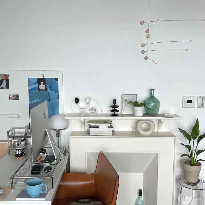 ホワイトとブラウンのトーンのモダンなホームオフィス、デスク、アームチェア、植物、壁飾りの暖炉が配置された雰囲気のあるインテリア