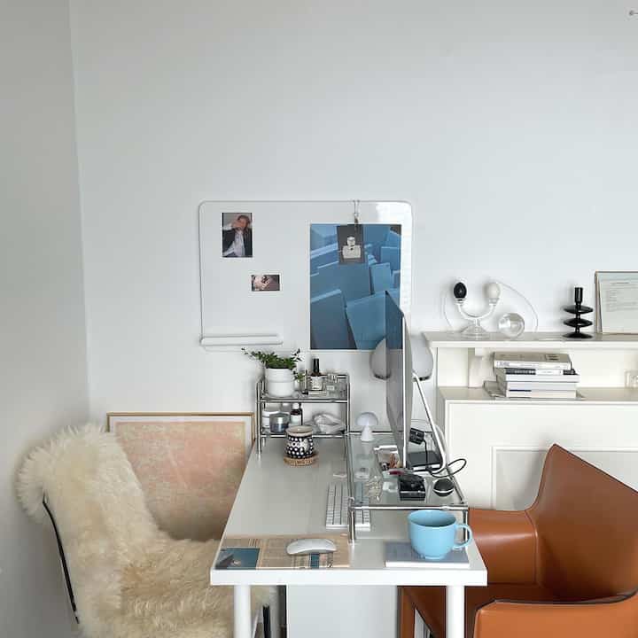 Bright white home office with a white desk, office chair, and monitor stand arranged neatly in a minimal setting