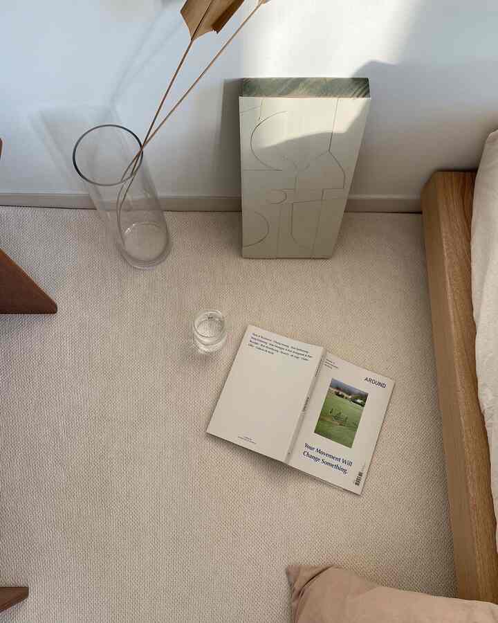 明るくナチュラルなベージュとホワイトのトーンの寝室の床とラグに、本とガラスの花瓶が置かれた落ち着いた空間