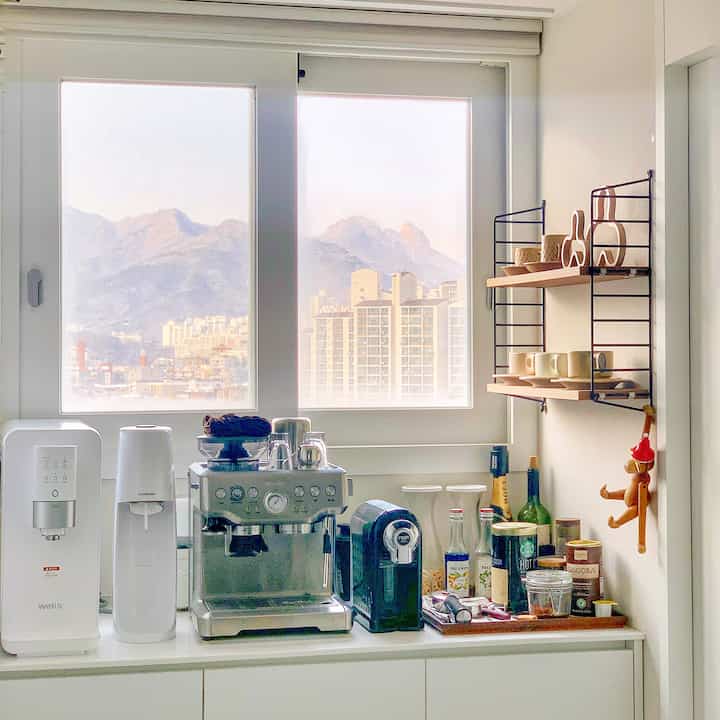 Bright white-toned veranda space featuring coffee machines and wall-mounted shelves in a mini home cafe interior