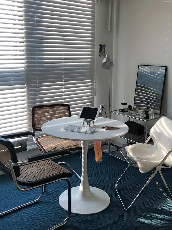 White round table with wood blinds and rattan armchairs in a natural modern style home office space