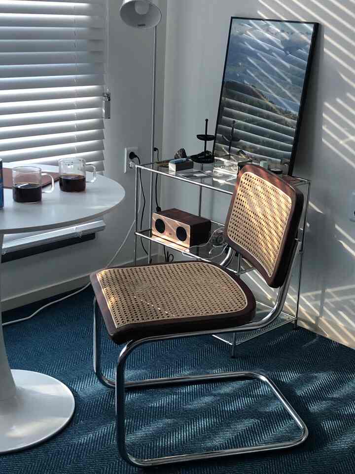 Navy rug flooring with wooden blinds casting light, featuring Cesca chair and side table in cozy home cafe setting