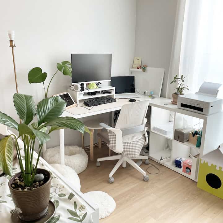 White and wood tone L-shaped home office featuring desks, an office chair, and plants in a cozy remote work setup