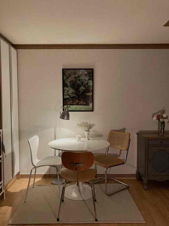 白い壁と木目調の床の小さなダイニングルーム、異素材の椅子と丸テーブルが配置された雰囲気のあるヴィンテージカフェ風インテリア