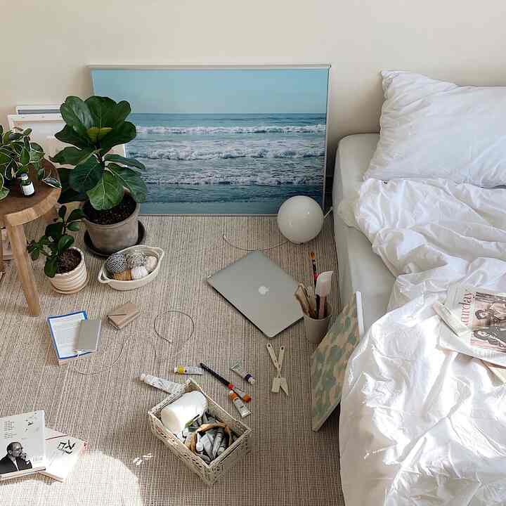 Bedroom in white and beige tones, featuring white bedding, plants, and a blue ocean poster for a natural atmosphere