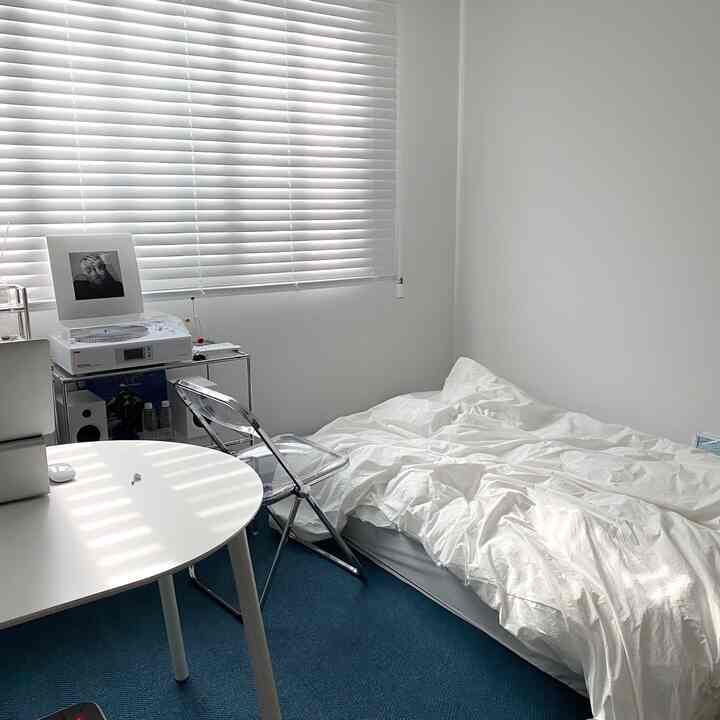 ホワイトとブルーのトーンの小さな寝室、白いベッドとデスク、透明な椅子が配置されたモダンで清潔感のあるインテリア