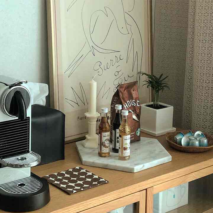 白と茶色のトーンのリビングのおうちカフェ、カプセルコーヒーマシンやラタンバスケット、植物が配置された温かみのある空間