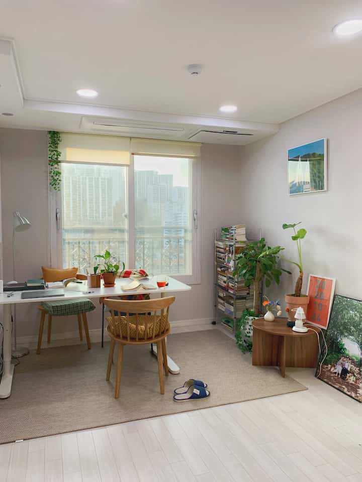 Bright white-toned small living room featuring wooden furniture and bookshelves with a natural and cozy home office atmosphere
