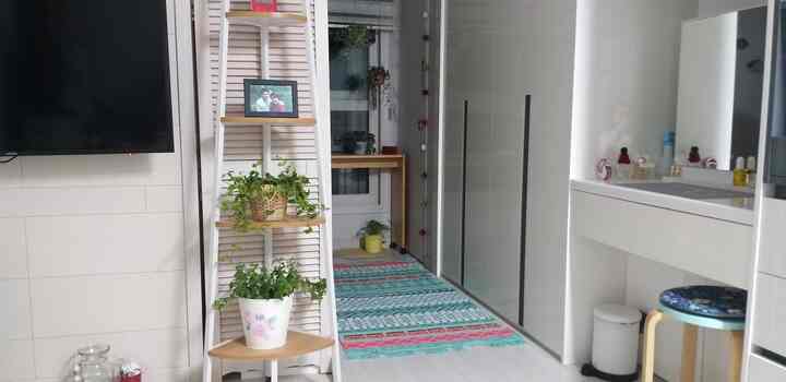 White and wood-toned studio apartment featuring multifunctional cabinets and plants in a cozy bedroom setting