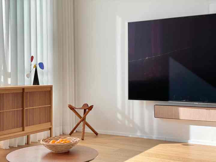 Minimal living room with white walls and wooden flooring, featuring a wall-mounted TV with beige soundbar and wooden cabinet.