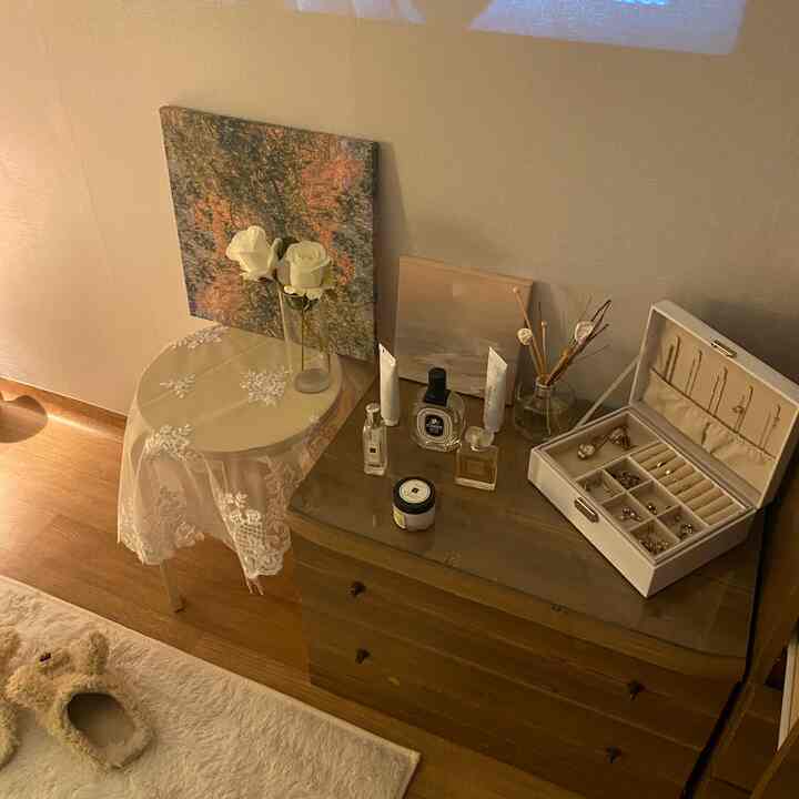 ホワイトレースのテーブルクロスと木目調のナイトテーブルが置かれた、ナチュラルで温かみのある寝室の一角、細やかな小物が配置された空間