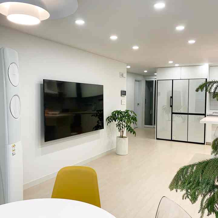 Bright white-toned living room and kitchen featuring yellow dining chair and green plants in a modern interior