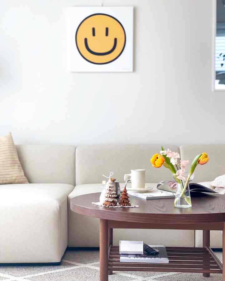 Bright beige and brown toned living room featuring a round wooden table, sofa, and a smiley face wall art in a cozy home cafe space