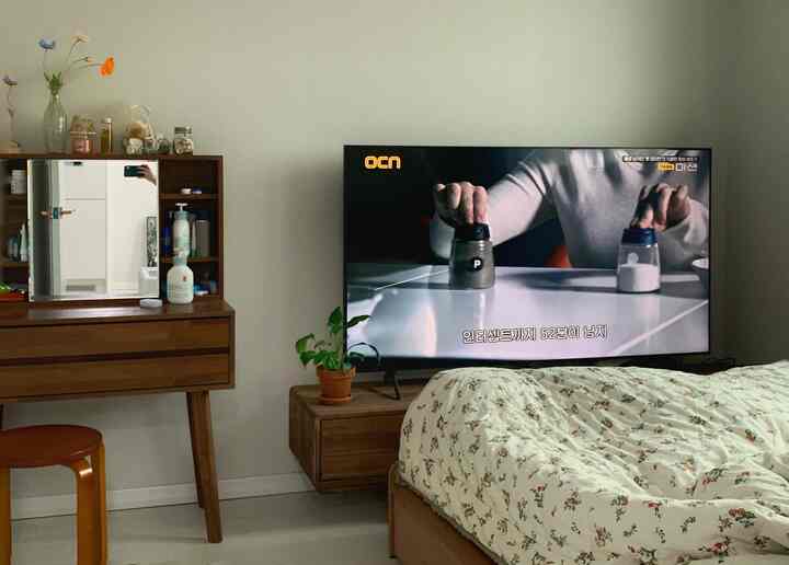 Natural wood-toned bedroom featuring floral bedspread, large TV, and vanity creating a cozy atmosphere
