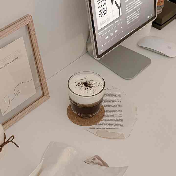 White-toned compact study space featuring desk with iPad, glass cup, and wooden picture frame offering a modern natural vibe