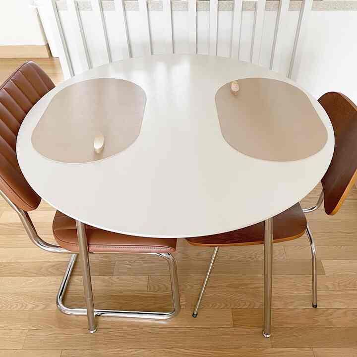 Simple and natural dining space with white round table and brown chairs for four people in warm wood-tone flooring