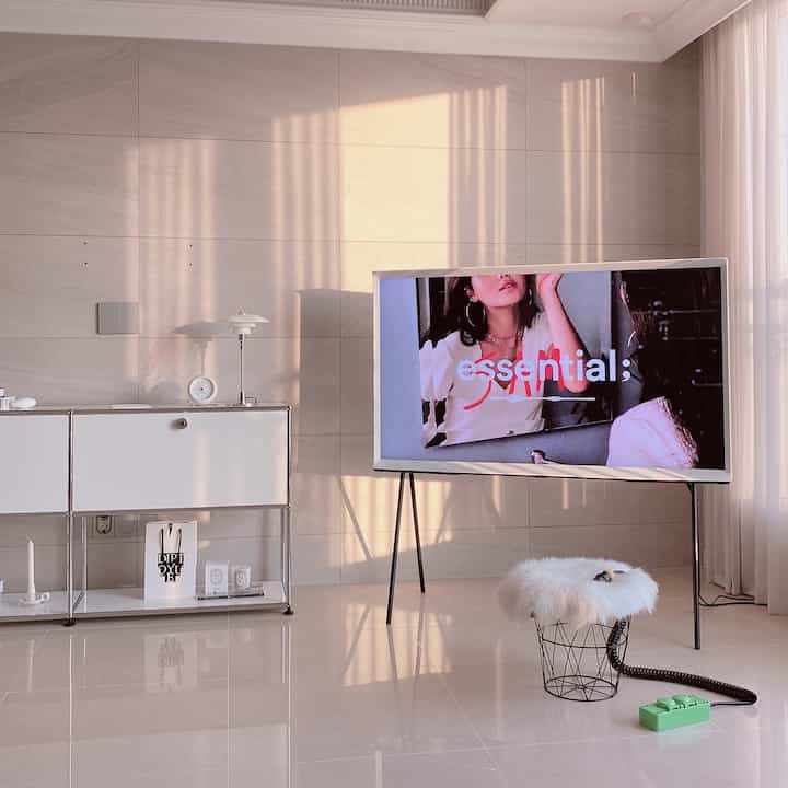 Bright living room in white and beige tones, featuring a simple table lamp, TV stand, and a green color multi-tap on the floor