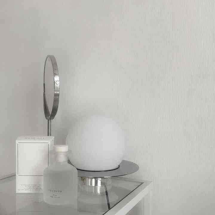 Minimalist space in bright white and silver tones featuring a spherical table lamp and diffuser on a glass surface