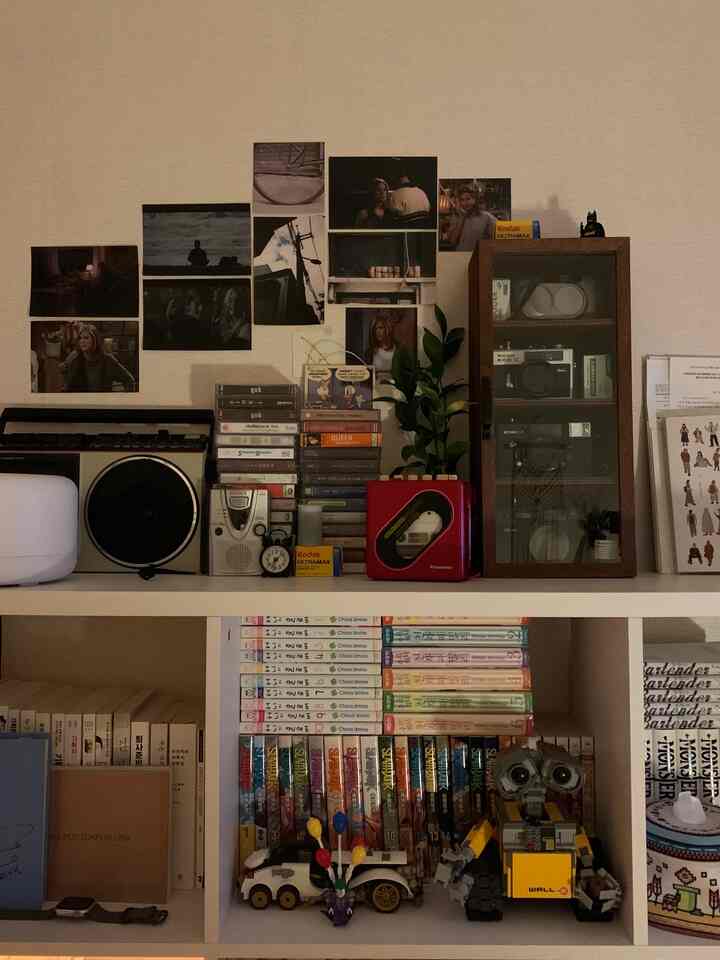 ベージュ色の壁と白い本棚が配置され、レトロな小物やヴィンテージカメラがある雰囲気のある収納空間