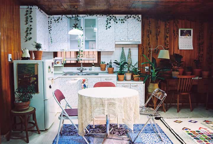 A warm kitchen space in white and wood tones featuring a round table with transparent and folding chairs arranged lovingly