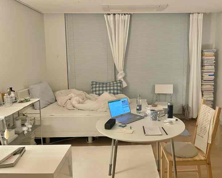 White and natural-toned studio bedroom featuring a round table and stacked books for a cozy atmosphere
