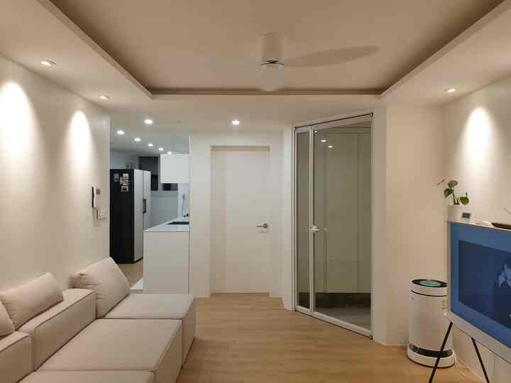 A modern entrance and living room in white and wood tones, featuring a sectional sofa and ceiling fan with a clean atmosphere